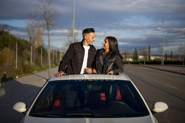 Giovane coppia guardando l'un l'altro mentre in piedi in auto tetto prendisole — Foto stock