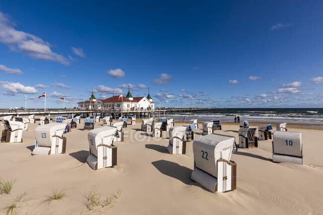 Germany, Mecklenburg-Western Pomerania, Heringsdorf, Hooded beach chairs on empty beach with Ahlbeck Pier in background — Stock Photo