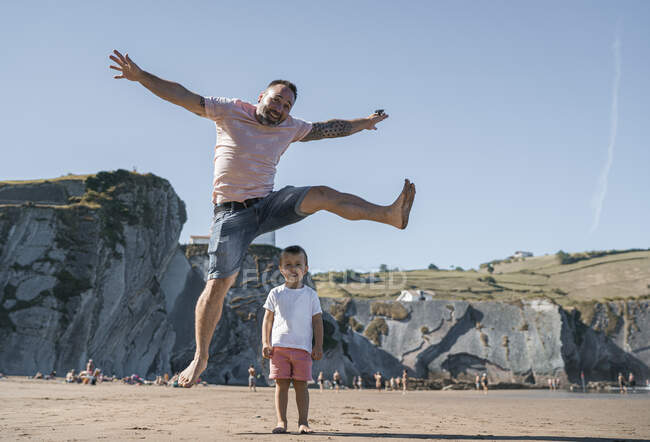 Cheerful father jumping over son at beach against sky — Stock Photo
