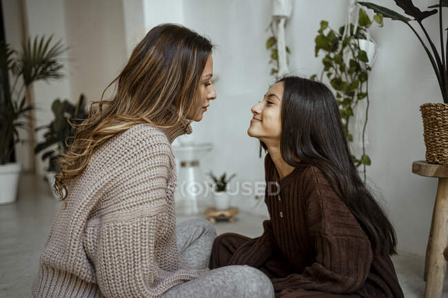 Sorridente madre e figlia seduta faccia a faccia a casa — Foto stock