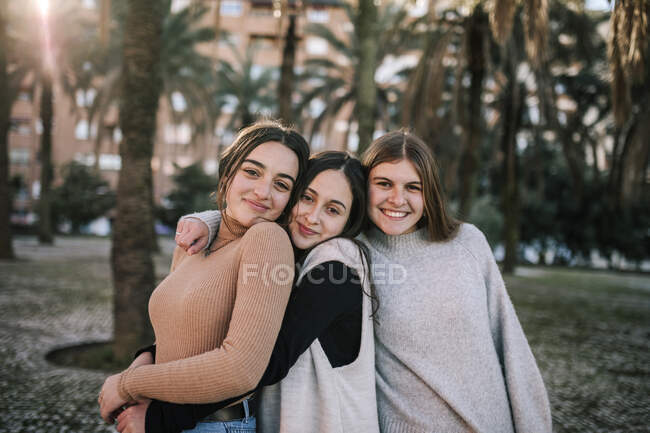 Female friends embracing while standing against trees in park — Stock Photo