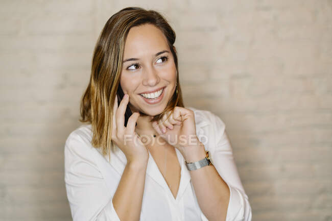 Sorridente donna d'affari che parla al cellulare contro il muro — Foto stock