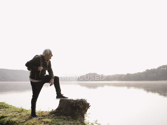 Старший чоловік з рюкзаком, який дивиться на озеро. — стокове фото