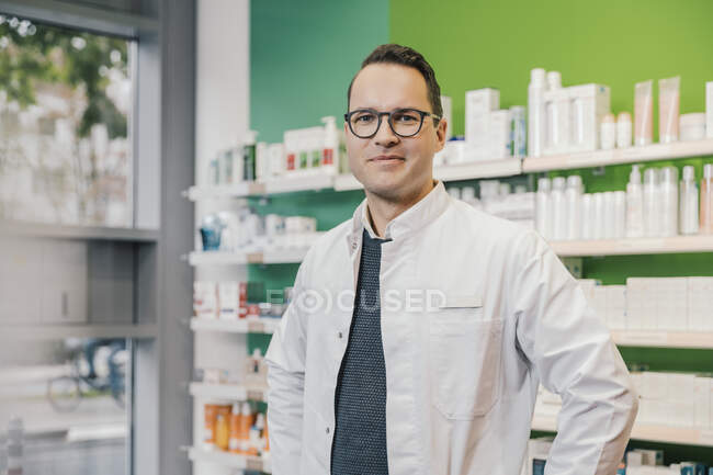 Pharmacien souriant portant une blouse de laboratoire alors qu'il se tenait dans un magasin de chimiste — Photo de stock