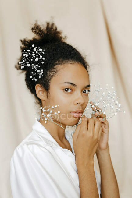 Mulher séria segurando flores brancas contra cortina bege — Fotografia de Stock