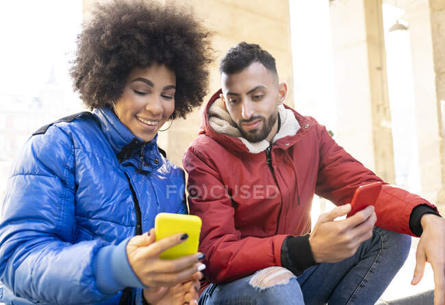 Усміхнена жінка показує другові мобільний телефон, сидячи надворі. — стокове фото