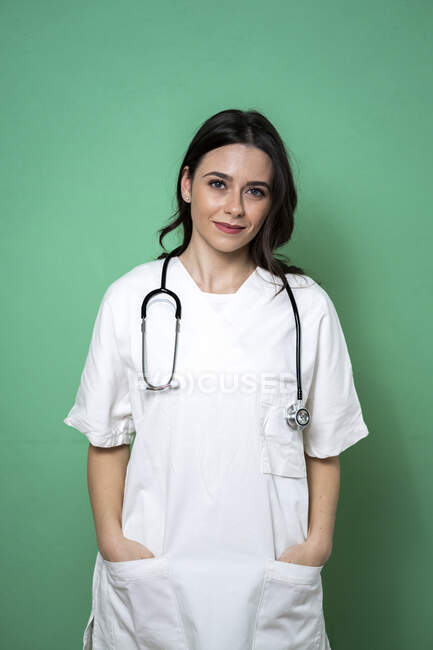Улыбающаяся женщина-врач с руками в карманах на зеленом фоне в студии — стоковое фото