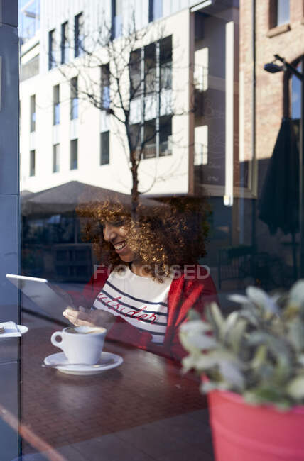 Mujer joven usando tableta digital mientras está sentado junto a la ventana en la cafetería - foto de stock