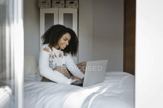 Donna sorridente che utilizza il computer portatile mentre seduto sul letto a casa — Foto stock