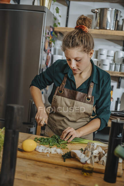 Junger Koch schneidet Schalotten auf Schneidebrett, während er in der Küche steht — Stockfoto