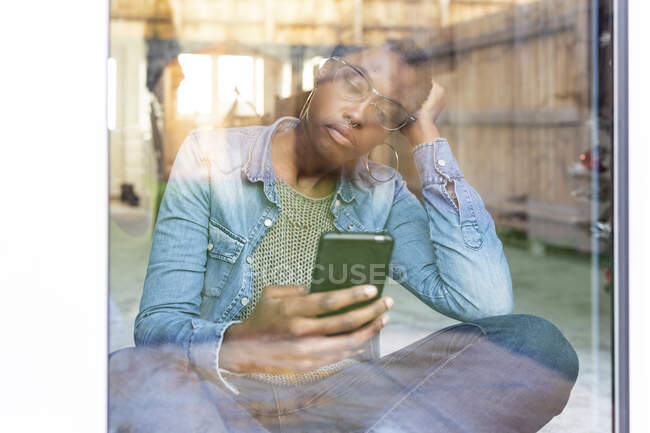 Triste femme assise par la fenêtre avec téléphone intelligent — Photo de stock