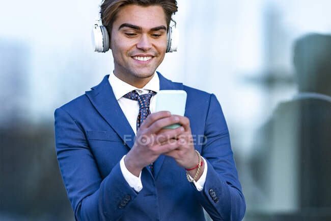Щасливий чоловік-професіонал використовує смартфон, слухаючи музику проти офісної будівлі — стокове фото