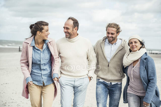 Group of adult friends walking side by side along sandy beach — Stock Photo