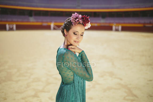 Flamenco dancer wearing blue dress and flowers posing while standing in bullring — Stock Photo
