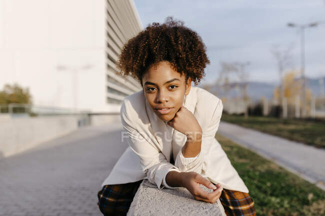 Довірлива молода жінка з волоссям афро сидить на стіні в місті. — стокове фото