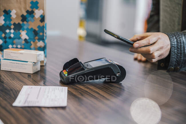 Mano del cliente con smart phone al banco cassa in farmacia — Foto stock