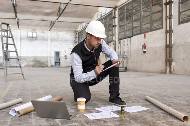 Male engineer analyzing site plan while kneeling on floor in building — Stock Photo