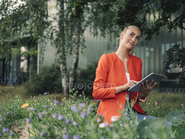Nachdenkliche Geschäftsfrau mit digitalem Tablet im Firmengarten — Stockfoto