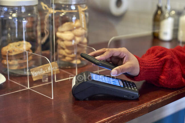 Mujer pagando a través del teléfono móvil en la cafetería - foto de stock