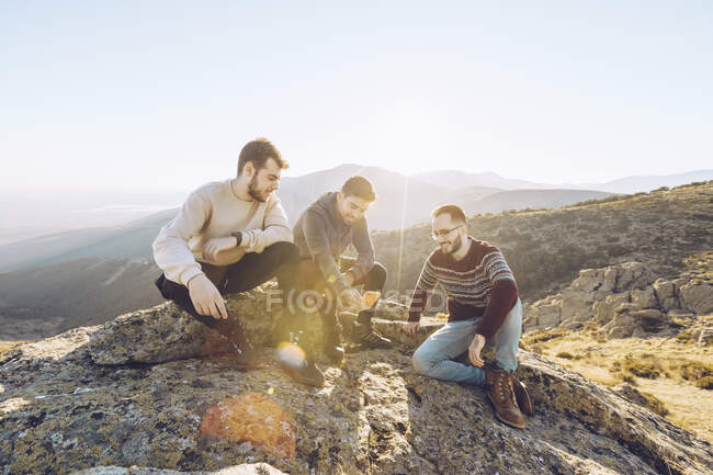 Male friends talking while sitting on mountain against clear sky during summer — Stock Photo