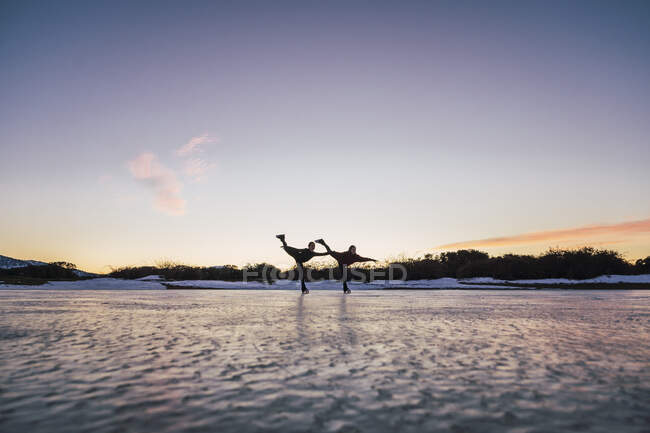 Silhuetas de dois patinadores femininos praticando juntos no lago congelado ao entardecer — Fotografia de Stock