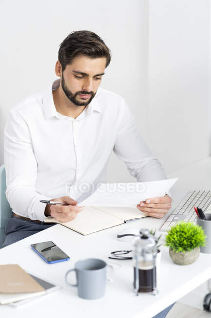Empresario masculino mirando el documento de papel mientras trabaja en el escritorio en la oficina - foto de stock