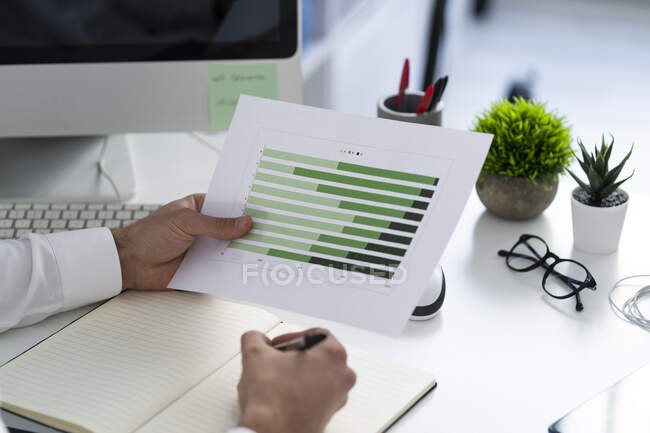 Empresario con documento gráfico en papel que trabaja sobre escritorio en el lugar de trabajo - foto de stock