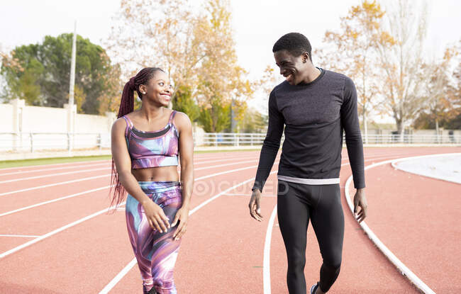 Hombre y mujer deportista feliz caminando en pista de atletismo durante el día soleado - foto de stock