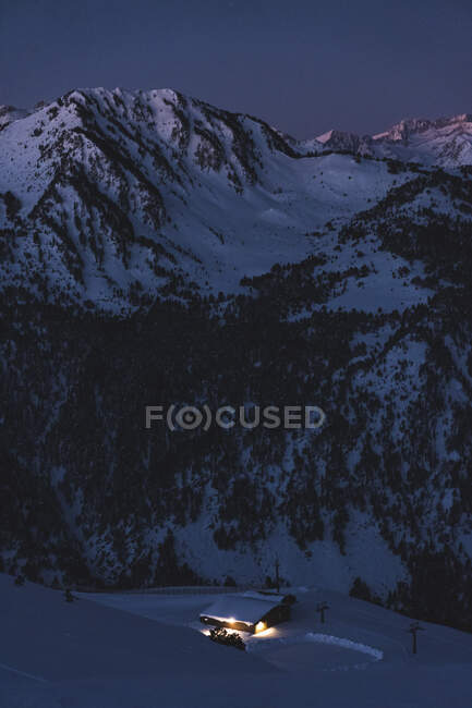 Beleuchtete Hütte am schneebedeckten Berg bei Sonnenaufgang — Stockfoto