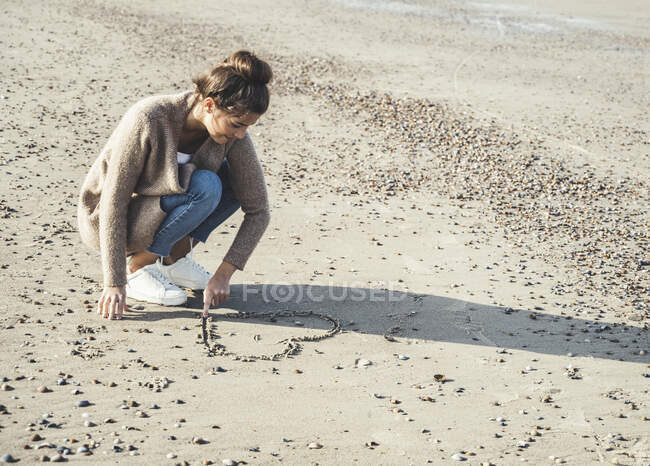 Giovane donna che disegna il cuore sulla sabbia in spiaggia — Foto stock