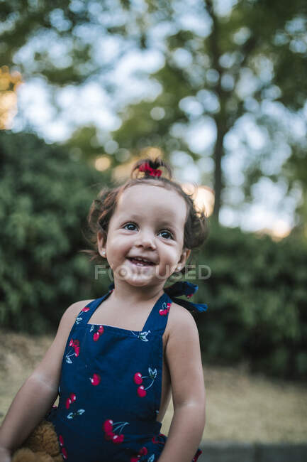 Щаслива маленька дівчинка відвернулася, стоячи навпроти дерев у парку. — стокове фото