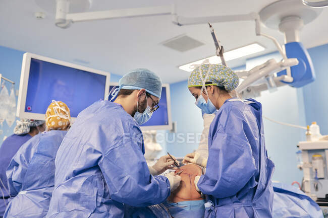 Doctors wearing face mask operating surgery while standing with colleague in background at operation room — Stock Photo
