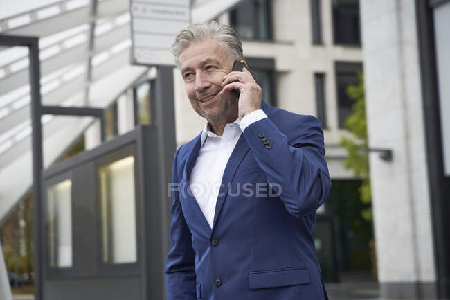 Empresário sorrindo falando no telefone celular enquanto espera na parada de ônibus na cidade — Fotografia de Stock
