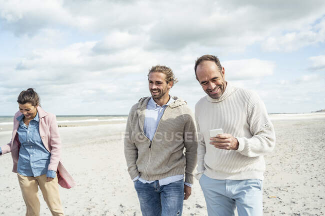 Due uomini che camminano e parlano fianco a fianco lungo la spiaggia sabbiosa — Foto stock