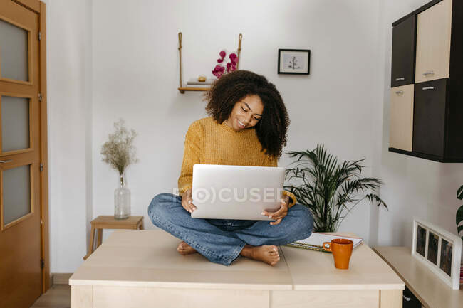 Young woman using laptop while sitting on table at home — Stock Photo