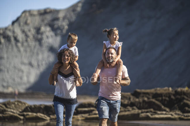 Parents carrying children on shoulder while walking at beach — Stock Photo