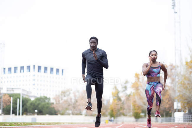 Deportista masculino y femenino corriendo en la pista contra el cielo despejado - foto de stock