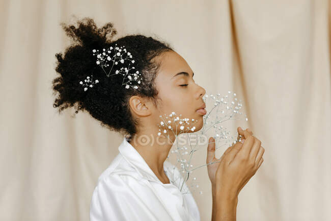 Frau mit geschlossenen Augen duftende weiße Blumen vor beigem Vorhang — Stockfoto