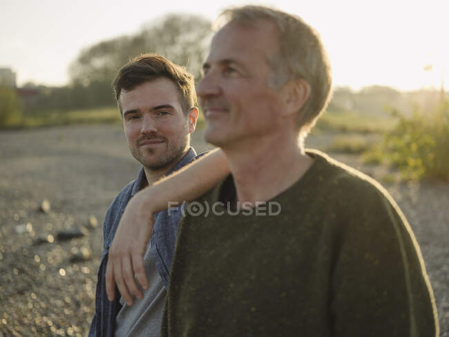 Son standing by thoughtful father at riverbank — Stock Photo