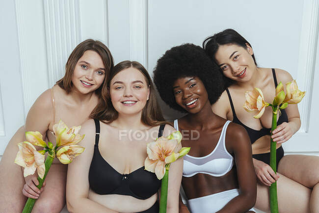 Прекрасна багатонаціональна група моделей моди в білизні з квітами проти білої стіни. — стокове фото