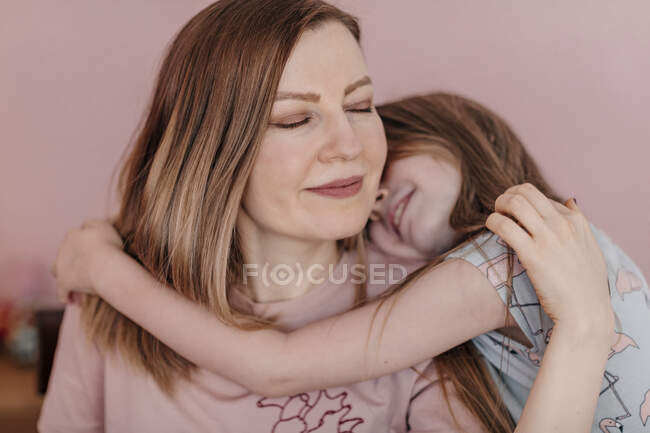 Figlia abbracciando madre contro muro a casa — Foto stock