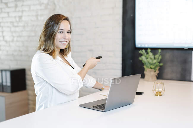 Sorridente donna d'affari che opera schermo di proiezione su telecomando in ufficio — Foto stock