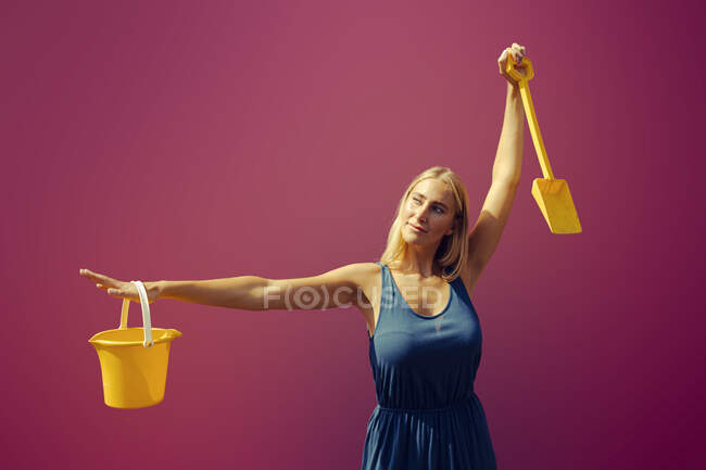 Giovane donna con secchio di sabbia e pala contro viola — Foto stock