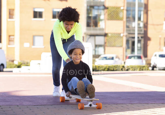 Сестра штовхає брата, який сидить на скейті під час гри на стежці. — стокове фото