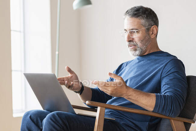 Homme d'affaires mature parlant sur appel vidéo par ordinateur portable tout en étant assis à la maison — Photo de stock