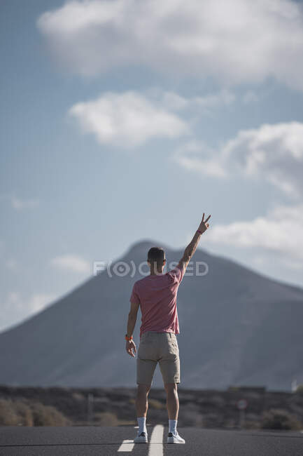 Чоловічий турист, який співає мир, стоячи на дорозі біля Лансароте у сонячний день (Іспанія). — стокове фото