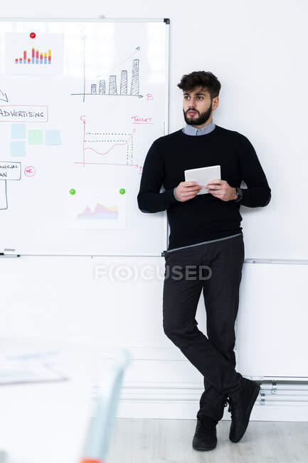 Homme d'affaires avec tablette numérique debout devant le tableau blanc dans le bureau — Photo de stock