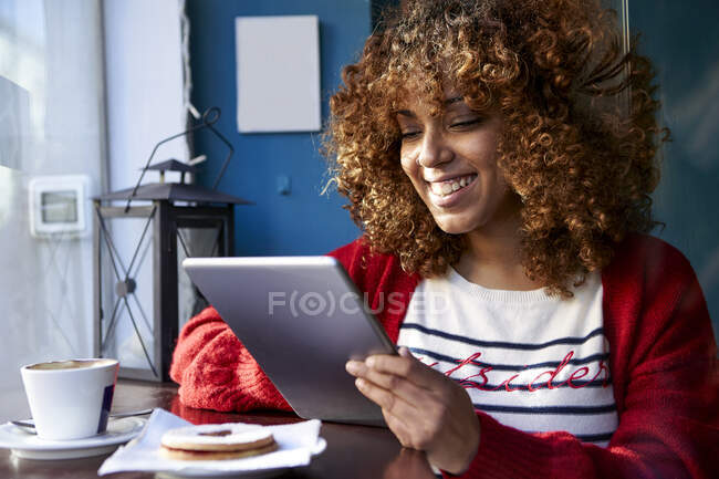 Улыбающаяся молодая женщина с помощью цифрового планшета, сидя в кафе — стоковое фото
