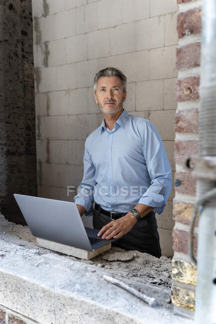 Architecte mature utilisant un ordinateur portable tout en se tenant debout sur le chantier de construction — Photo de stock