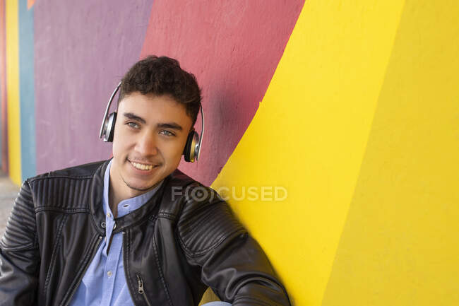 Uomo felice in giacca di pelle guardando lontano mentre ascoltava musica da parete multicolore — Foto stock